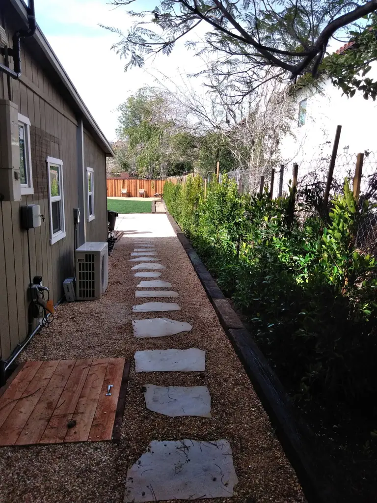 A finished side yard — flagstone stepping stones set into gravel, running between the house and a clipped hedge