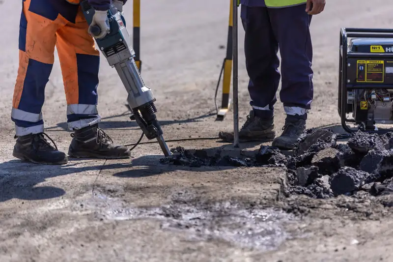 A pneumatic breaker splitting up a concrete slab, with the broken sections lifted clear alongside
