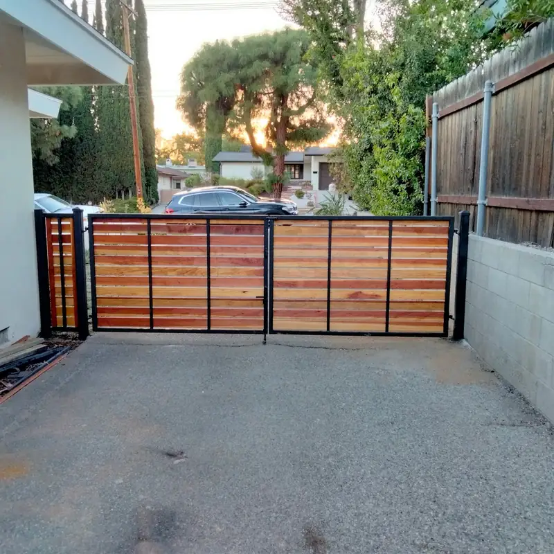 A finished redwood horizontal-slat driveway gate on a black steel frame, lit by evening sun