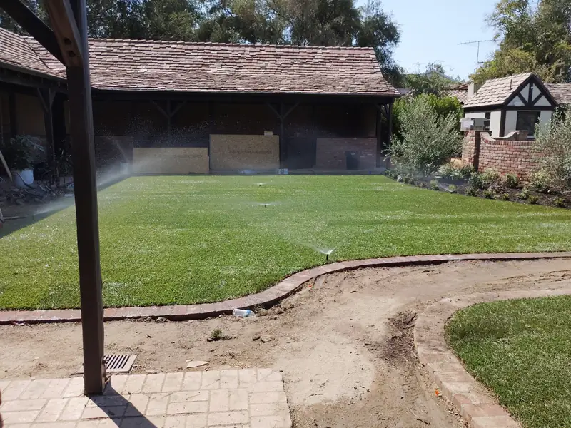 Pop-up sprinklers running across a newly laid lawn in front of a house, throwing overlapping arcs of water