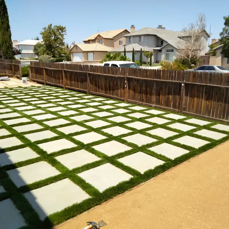 Large square concrete pavers laid in a grid with strips of turf between them, filling a side yard from fence to fence