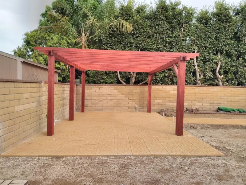 A redwood pergola built over a finished paver patio, enclosed by a block wall